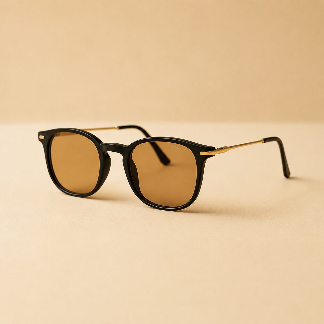 Black sunglasses with brown lenses and gold temples resting on a beige surface, product photo